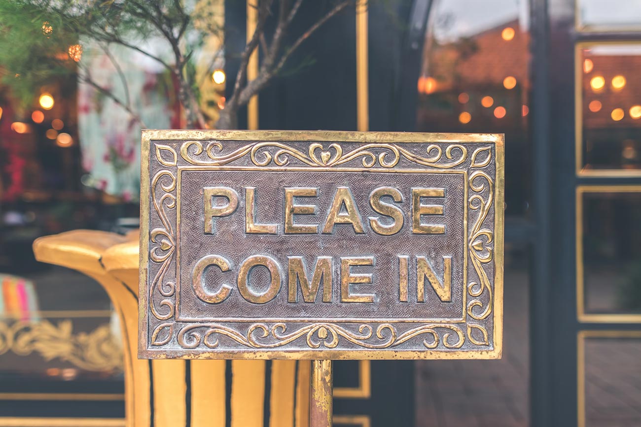 A sign in front of a storefront that says Please Come In